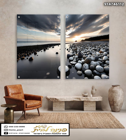 Two-panel glass wall art featuring a dramatic sunset over a pebble beach with dark clouds, smooth water, and rounded stones in black, white, and gray tones.